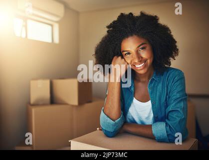 Solo qualche scatola in più da andare. Ritratto di una giovane donna allegra che riposa sulla sua mano mentre è circondato da scatole di cartone il giorno in movimento all'interno a. Foto Stock