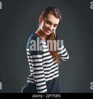 Niente la impedisce di sorridere. Studio shot di una giovane donna allegra che tiene il collo in piedi su uno sfondo scuro. Foto Stock