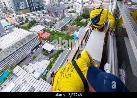 Lavoratori thailandesi che riparano le finestre su un alto grattacielo sopra Bangkok, Thailandia Foto Stock