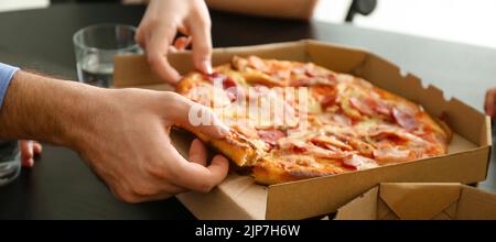 Persone che mangiano pizza fresca a tavola in ufficio, primo piano Foto Stock