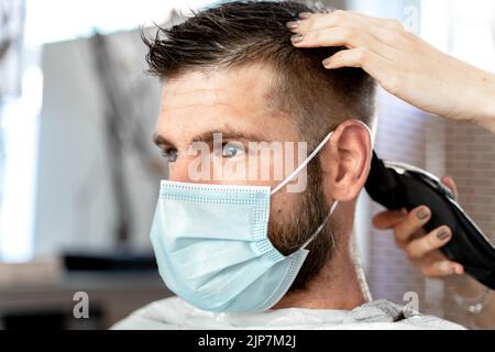 Vista ravvicinata della mano di un parrucchiere che regola i capelli di un uomo in un salone Foto Stock