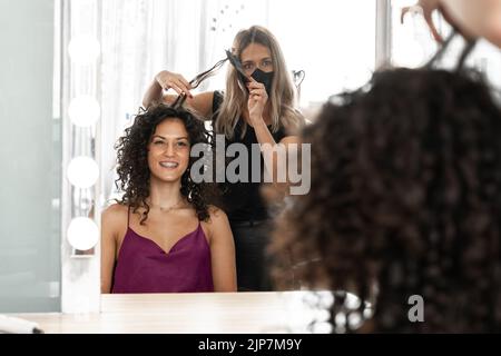 Parrucchiere con maschera che pettina i capelli di una donna in un salone Foto Stock