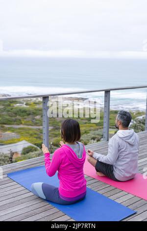 Felice coppia diversa fare yoga insieme, meditando sul balcone Foto Stock