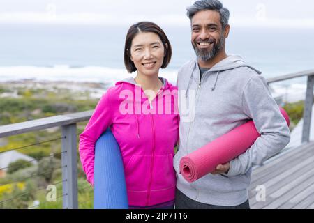 Felice coppia diversa fare yoga insieme, tenendo tappetini yoga sul balcone Foto Stock