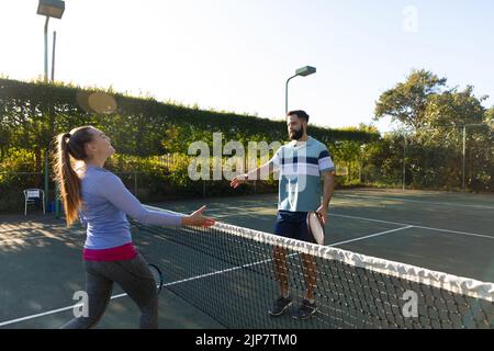 Felice coppia caucasica giocare a tennis scuotendo le mani su Internet sul campo da tennis all'aperto Foto Stock