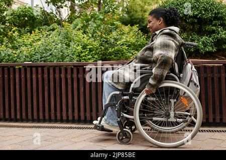 Vista laterale ritratto di donna nera sorridente con disabilità nel giardino autunnale della città, spazio copia Foto Stock
