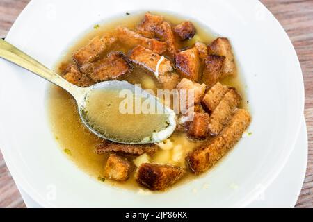 Zuppa d'aglio con pane arrosto a fette e formaggio e cucchiaio in piatto bianco, spicchio. Cucina tradizionale della repubblica Ceca. Foto Stock