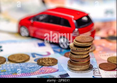 Torre con monete in euro sullo sfondo di banconote e giocattolo rosso auto, prestito e concetto di assicurazione Foto Stock