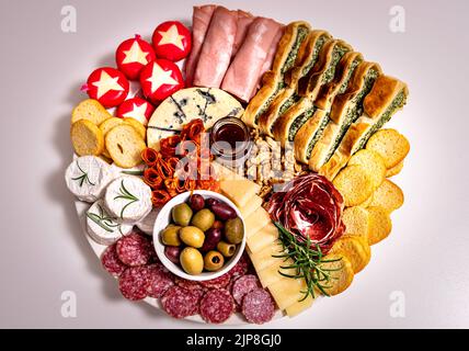 Vista dall'alto del pranzo o dell'antipasto con un piatto con salame, peperoni, formaggio brie, prosciutto. Veduta aerea di un plat: Pasto composto da salumi e noci Foto Stock