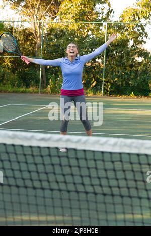 Felice donna caucasica che gioca a tennis celebrando sul campo da tennis all'aperto Foto Stock