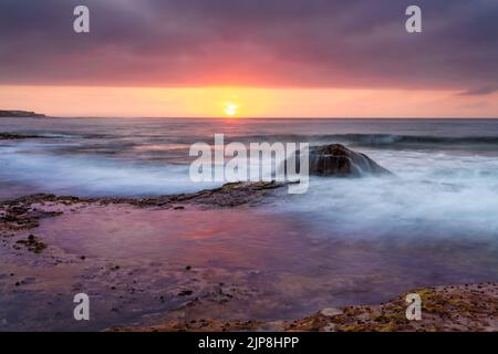 Le nuvole di tempesta incombono su Boat Harbour mentre il sole illumina il cielo di rosso e giallo Foto Stock