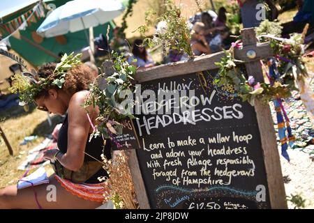 I bambini e le donne giovani che fanno gli abiti-testa nel hedgerow-abiti stand testa in Wild Tribe zona. Scene del festival orientato alla famiglia Camp Bestival, Lulworth Castello e Estate, Dorset 28 - 31 2022 luglio Foto Stock