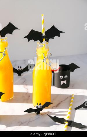 Halloween mocktail. Cocktail analcolico all'arancia per la festa di Halloween su un tavolo bianco. Le cannucce sono decorate con pipistrelli di carta tagliati. Halloweens spooky Foto Stock