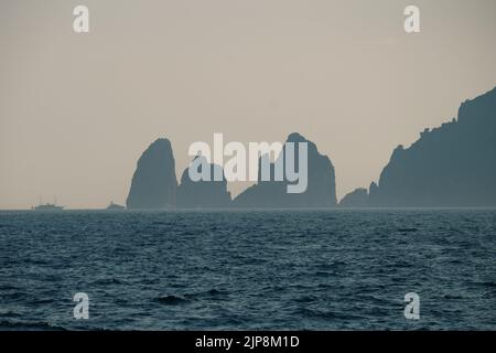 Capri faraglioni Wave erosione formazioni rocciose stagni dell'isola di Capri Italia nella baia di Napoli vista nella nebbia marina con barche da diporto. Foto Stock