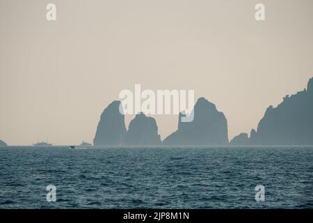 Capri faraglioni Wave erosione formazioni rocciose stagni dell'isola di Capri Italia nella baia di Napoli vista nella nebbia marina con barche da diporto. Foto Stock