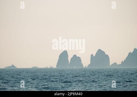 Capri faraglioni Wave erosione formazioni rocciose stagni dell'isola di Capri Italia nella baia di Napoli vista nella nebbia marina con barche da diporto. Foto Stock