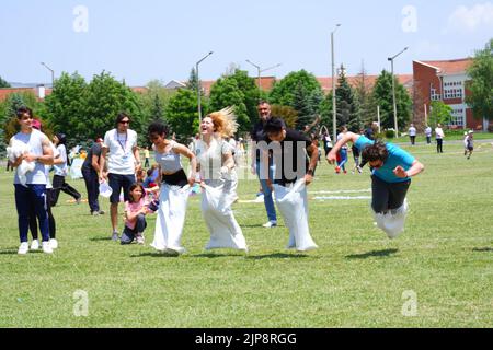 Le persone e i bambini si divertono a correre in gunnysack in estate all'aperto Foto Stock