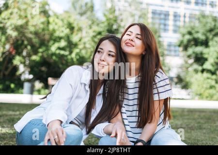 Giovani belle ragazze asiatiche con capelli lunghi in abiti casual, amici che si divertono nel parco cittadino Foto Stock