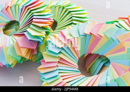 Gli anelli Origami in fogli di carta colorati collegati giacciono su un tavolo di legno bianco, foto ravvicinata con messa a fuoco morbida selettiva Foto Stock