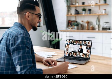 Formazione online. Guarda sopra la spalla di un tipo di gara mista prendendo appunti in un notebook, sullo schermo di un computer portatile con un insegnante e un gruppo di studenti multirazziali. E-learning, webinar, lezione online Foto Stock