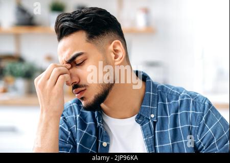 Il concetto di affaticamento, emicrania, cefalea. Primo piano di un uomo indiano o arabo stanco esausto che massaggia il ponte del naso, che ha un mal di testa, emicrania, ha chiuso la testa, ha bisogno di riposo Foto Stock