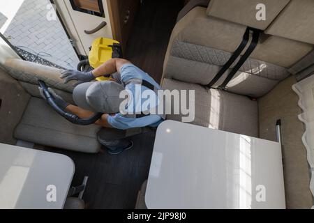 Vista aerea di Caucasian pulizia servizi lavoratore con cura Vacuuming il tessuto finitura della zona soggiorno nel moderno veicolo ricreativo. Auto RV Foto Stock