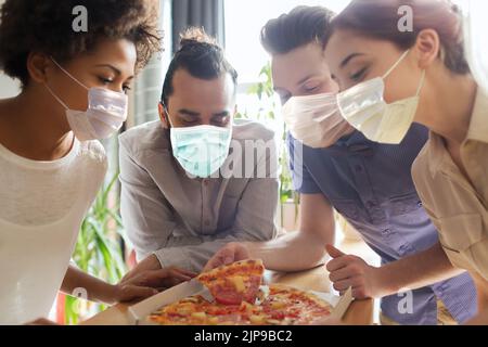 team di lavoro che mangia in maschere pizza in ufficio Foto Stock