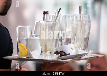 Amburgo, Germania. 16th ago, 2022. Un cameriere dell'Alsterarkaden porta con sé un vassoio con bicchieri usati e bottiglie vuote. Credit: Jonas Walzberg/dpa/Alamy Live News