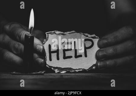 Carta di cartone con testo di aiuto nelle mani di una donna Ucraina vicino a una candela al buio su un tavolo a casa, un messaggio di aiutare l'Ucraina nel Foto Stock