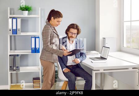 Due dipendenti che lavorano in ufficio e che guardano alcuni documenti aziendali negli appunti Foto Stock