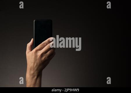 Vista posteriore della mano dell'uomo che tiene lo smartphone isolato su sfondo scuro con spazio copia Foto Stock