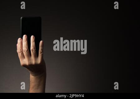 Vista posteriore della mano dell'uomo che tiene lo smartphone isolato su sfondo scuro con spazio copia Foto Stock