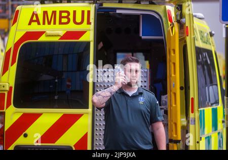 Un operaio di ambulanza prende una pausa durante un turno durante il tempo caldo di estate. Il servizio di ambulanza è sotto pressione con un carico di lavoro aumentato. Foto Stock