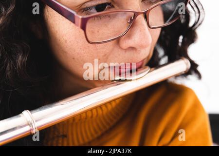Primo piano di una donna bruna che indossa un maglione giallo e che gioca un flauto trasversale Foto Stock