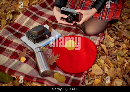 Plaid rosso e giallo a scacchi e foglie autunnali, libro, thermos in metallo argentato e vecchia fotocamera retrò Foto Stock