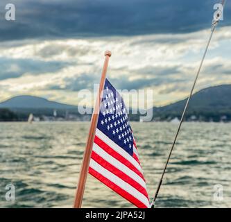 Una bandiera americana a poppa di una barca a vela con un lontano Camden Maine sullo sfondo Foto Stock