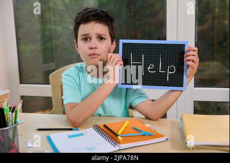 Adorabile schoolboy punti con matita su una lavagna con iscrizione Aiuto. Nuovo semestre accademico. Ritorno a scuola Foto Stock