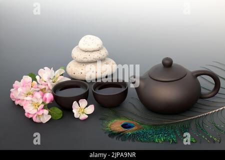 Cerimonia del tè giapponese per la pace interiore con impacchi di ciottoli, set da tè in ceramica, fiori di fiori di mela, piume di pavone. Concetto di equilibrio e consapevolezza Zen Foto Stock