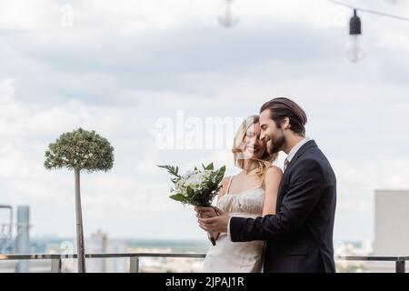 Giovane sposo mano toccante di sposa con bouquet sulla terrazza Foto Stock