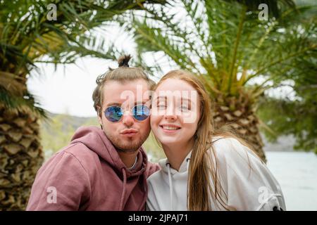 Una bella coppia caucasica che si posa di fronte alle palme durante le loro vacanze Foto Stock