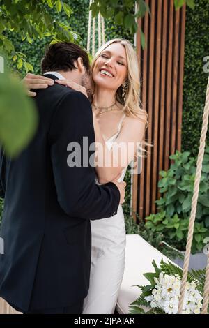 Sposarsi in abito baciare collo di sposa vicino bouquet sulla terrazza del ristorante Foto Stock