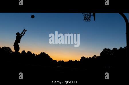 Norimberga, Germania. 16th ago, 2022. Un giovane gioca a basket in un cerchio pubblico sotto un ponte al crepuscolo. Credit: Daniel Karmann/dpa/Alamy Live News Foto Stock