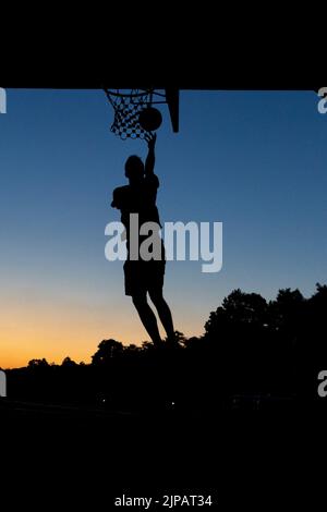 Norimberga, Germania. 16th ago, 2022. Un giovane gioca a basket in un cerchio pubblico sotto un ponte al crepuscolo. Credit: Daniel Karmann/dpa/Alamy Live News Foto Stock