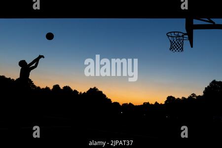 Norimberga, Germania. 16th ago, 2022. Un giovane gioca a basket in un cerchio pubblico sotto un ponte al crepuscolo. Credit: Daniel Karmann/dpa/Alamy Live News Foto Stock