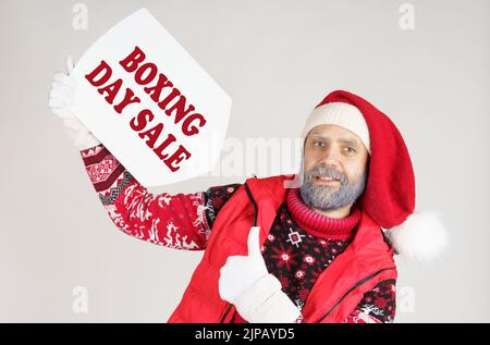 Concetto di natale e Capodanno. Babbo Natale sta tenendo un segno bianco con l'iscrizione - Boxing Day sale. Con la mano sinistra, mostra un gesto di classe. Foto Stock