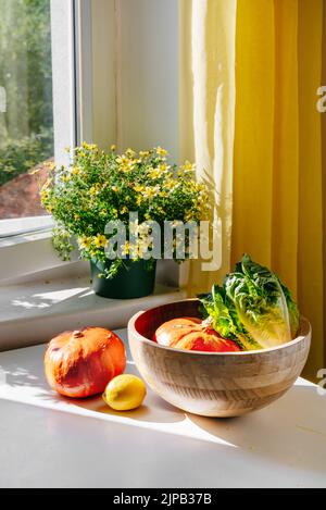 Verdure - Punpkin, insalata verde - in una ciotola di bambù su un tavolo bianco di fronte alla finestra con luce naturale. Luce solare. Concetto di zero sprechi. Acquista cibo biologico locale Foto Stock