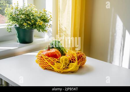 NET bag con zucche di verdure e insalata verde sul tavolo da cucina di fronte alla finestra. Nessun spreco e nessuna plastica libera Foto Stock