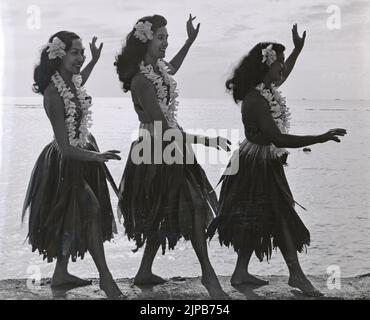 Tre giovani donne hawaiane che indossano costumi da ballo hula tradizionali che eseguono una tradizionale danza hula sulla spiaggia, Hawaii, USA T. Foto Stock