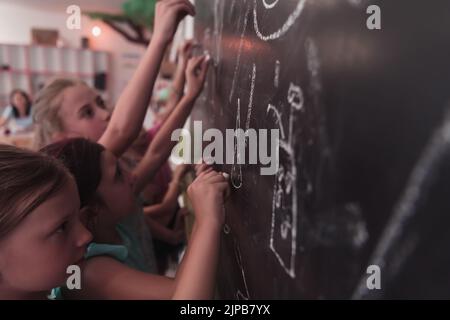 I bambini scrivono e disegnano sulla lavagna nella scuola elementare mentre imparano le basi dell'istruzione Foto Stock