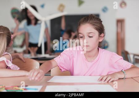 Bambine che si siedono nella scuola elementare disegnando su carta con i loro amici mentre si siedono in una classe moderna Foto Stock